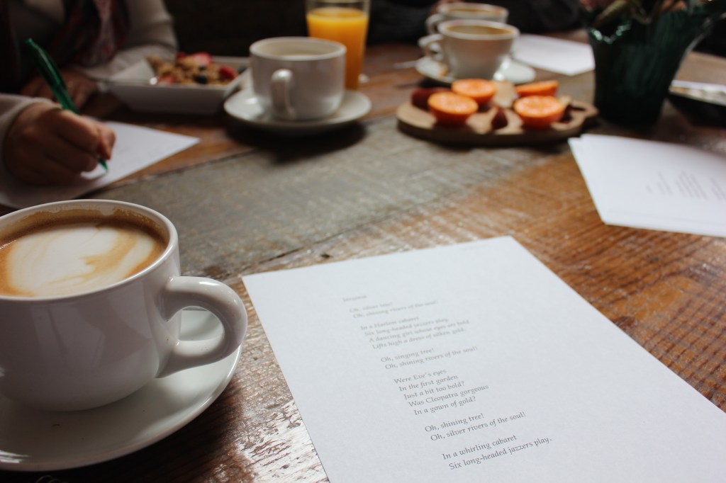 A group of "Coffee with Langston" attendees discuss a chosen poem amid food and drink.